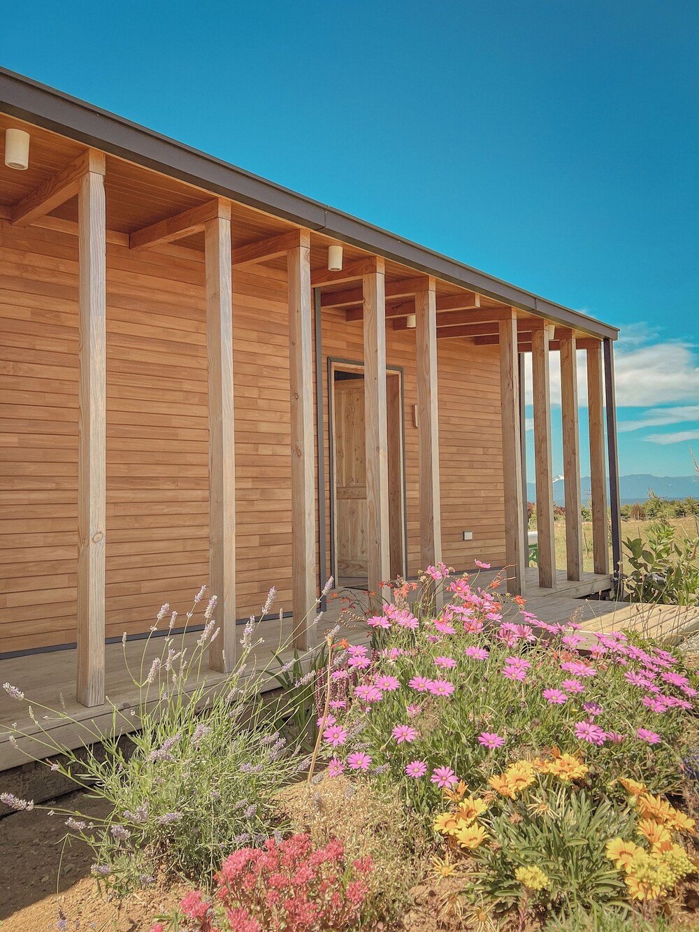 Wooden building with covered porch and garden of flowers