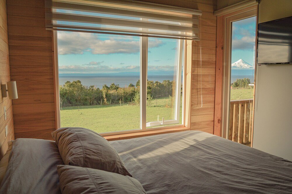 Bedroom with large window onto grassy field and distant mountain