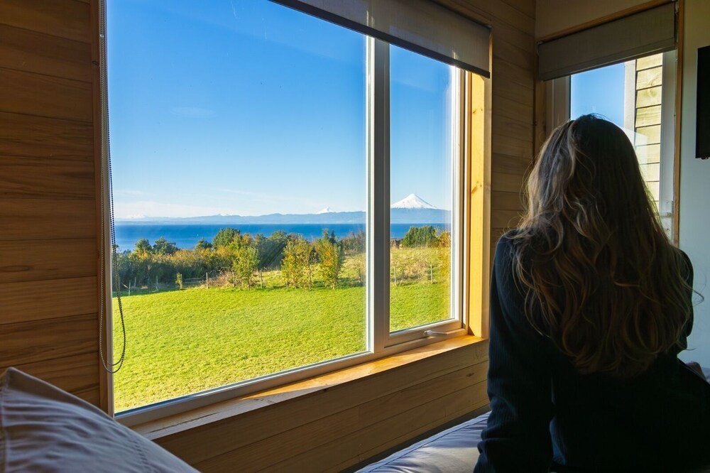 Room with large window facing green field, trees and mountain