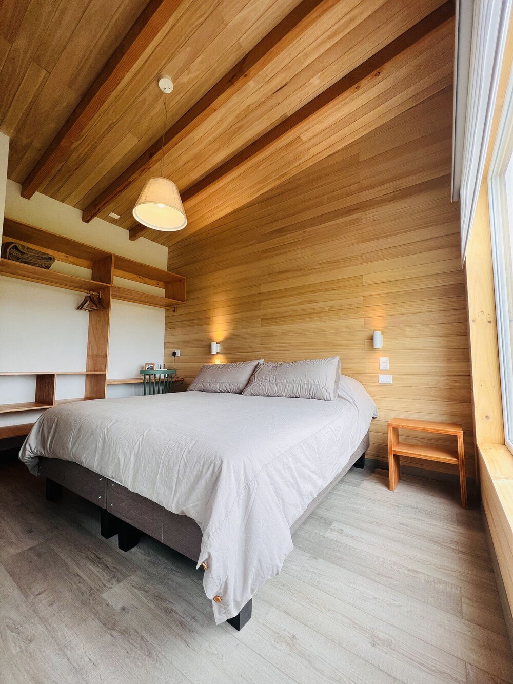 Bedroom with wooden ceiling, grey bedspread and bedside lamps