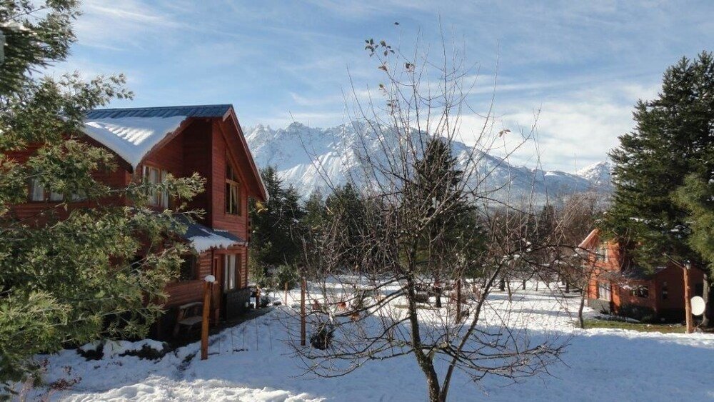 Wooden cabin with a snow-covered yard and mountains behind