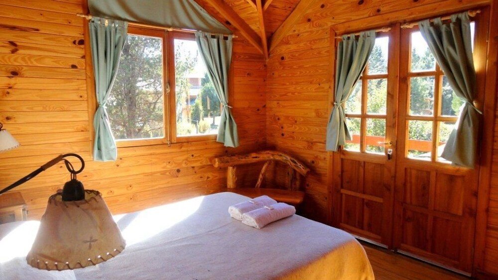 Wooden cabin room with a bed, a lamp and curtained windows