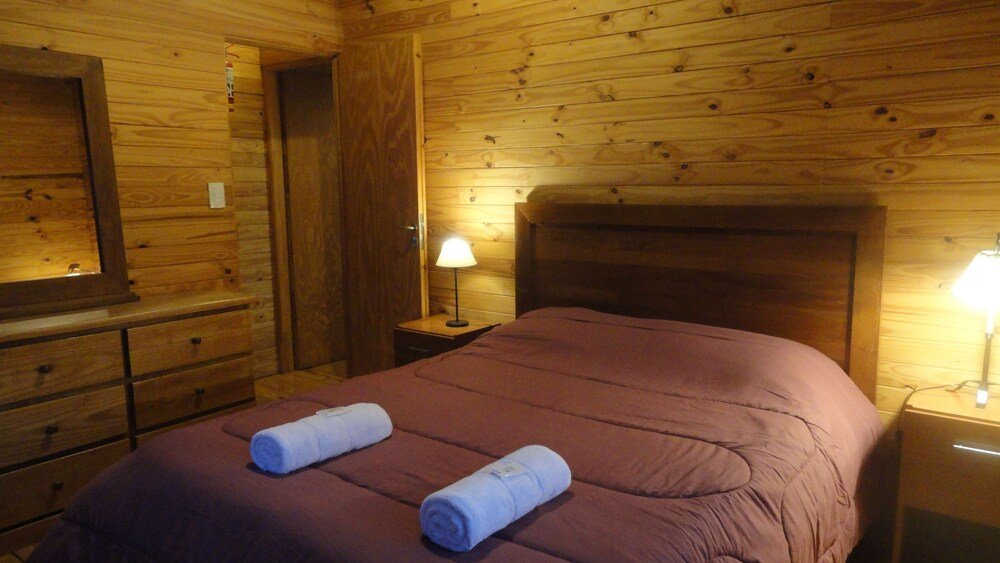 Wooden cabin room with a bed, a nightstand, a lamp and a mirror
