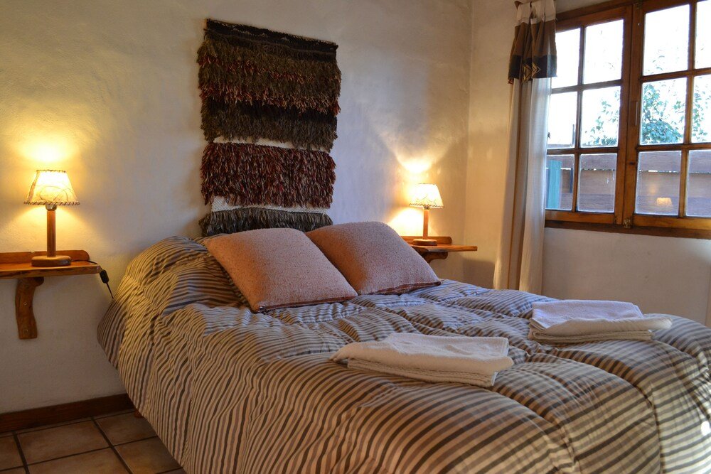 Cama tendida con ropa de cama a rayas, dos lámparas y un tapiz