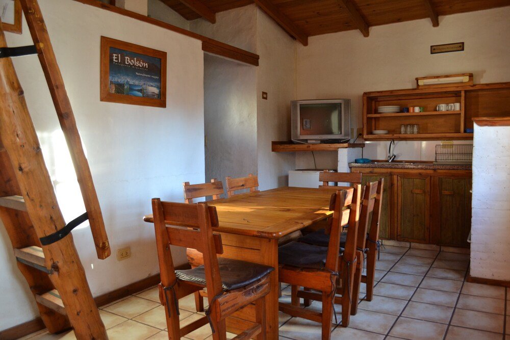 Wooden dining table with chairs, a television and a kitchen area