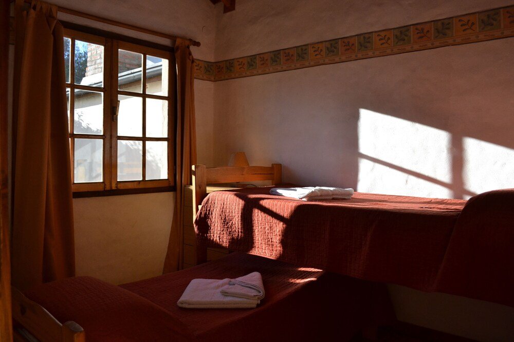 Room with a single bed, a small table and a curtained window