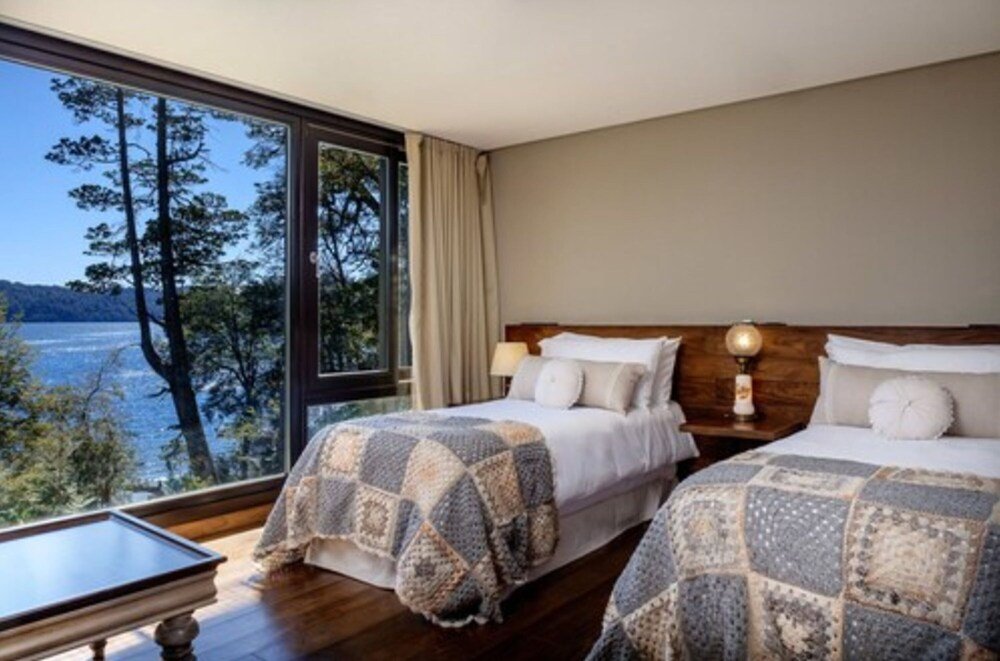 Dormitorio con dos camas, lámpara en la mesa de luz y vista al lago