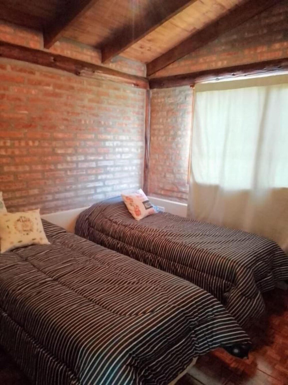 Habitación con dos camas, pared de ladrillo y ventana con cortinas
