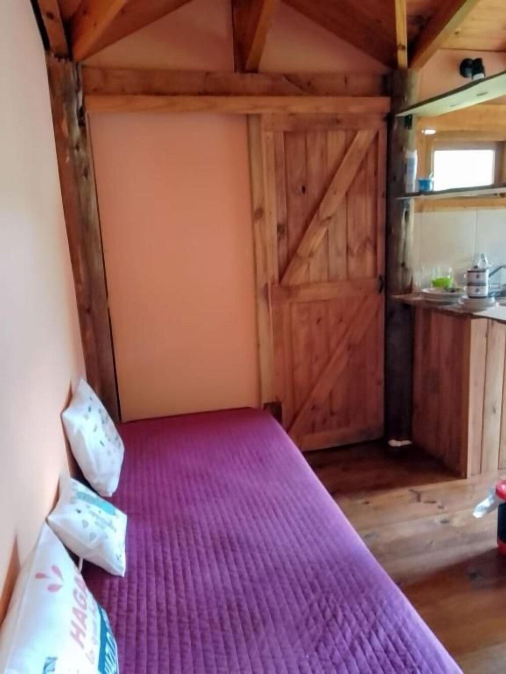 Interior de madera con cama, almohadas y sector de cocina