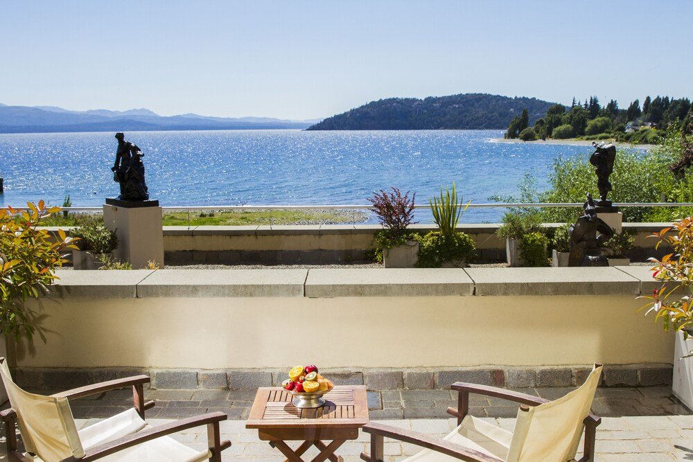 Patio con mesa y sillas con vista a un lago, estatuas y cerámicas