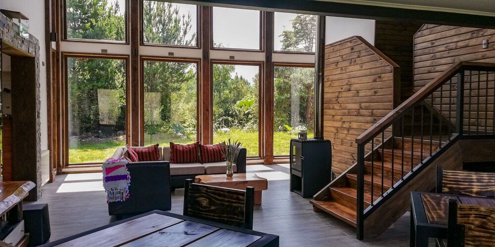 Modern lodge interior with large windows, wooden staircase and seating area