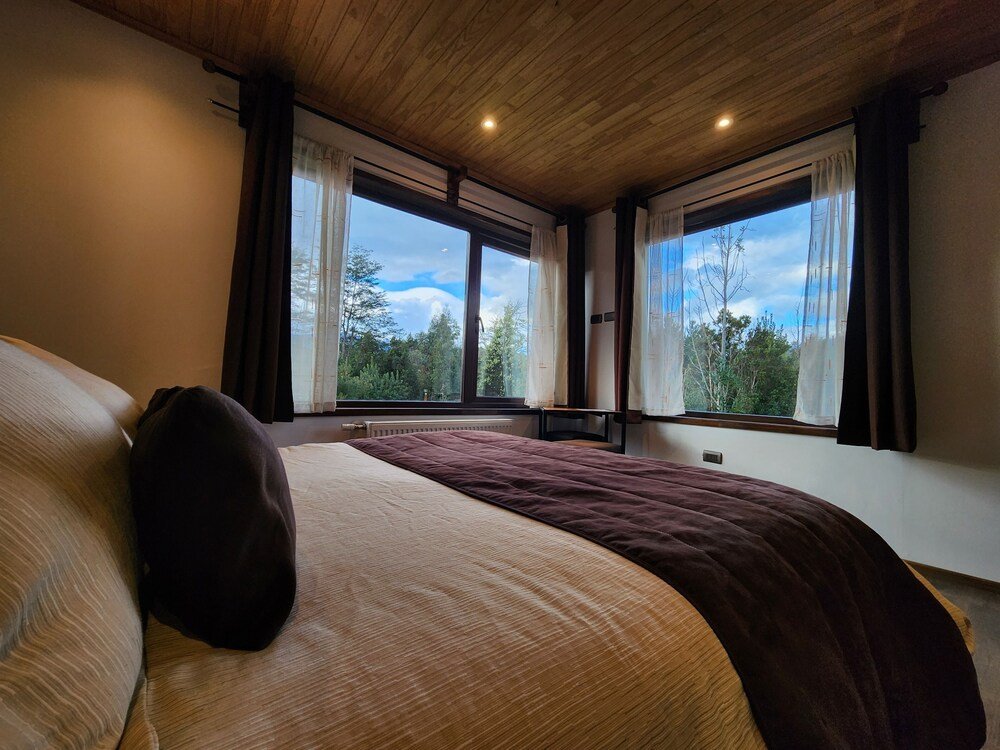 Bedroom with large bed, curtained windows and wooden ceiling