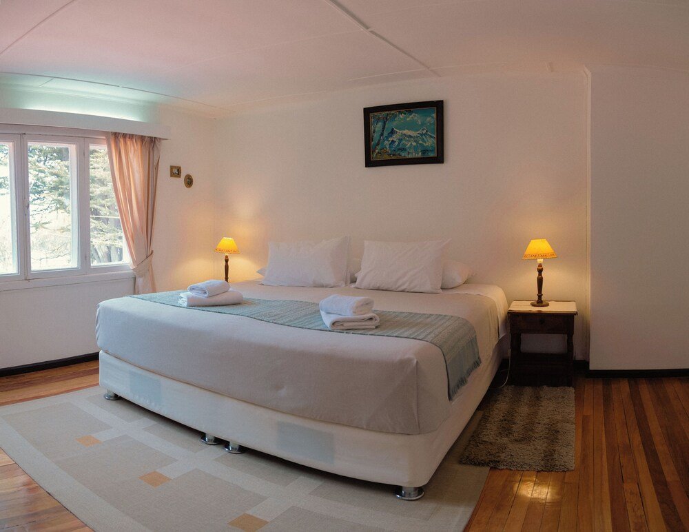 Cama tendida con ropa blanca y dos lámparas de mesa de luz
