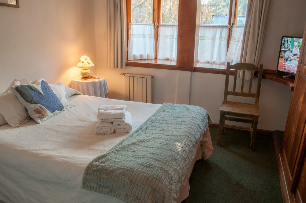 Neatly made bed with pillows, a rolled towel and a blanket
