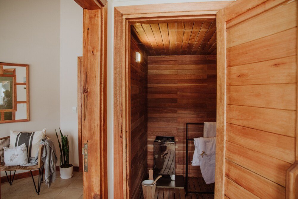 Sala de madera tipo sauna con banco, planta y toallero