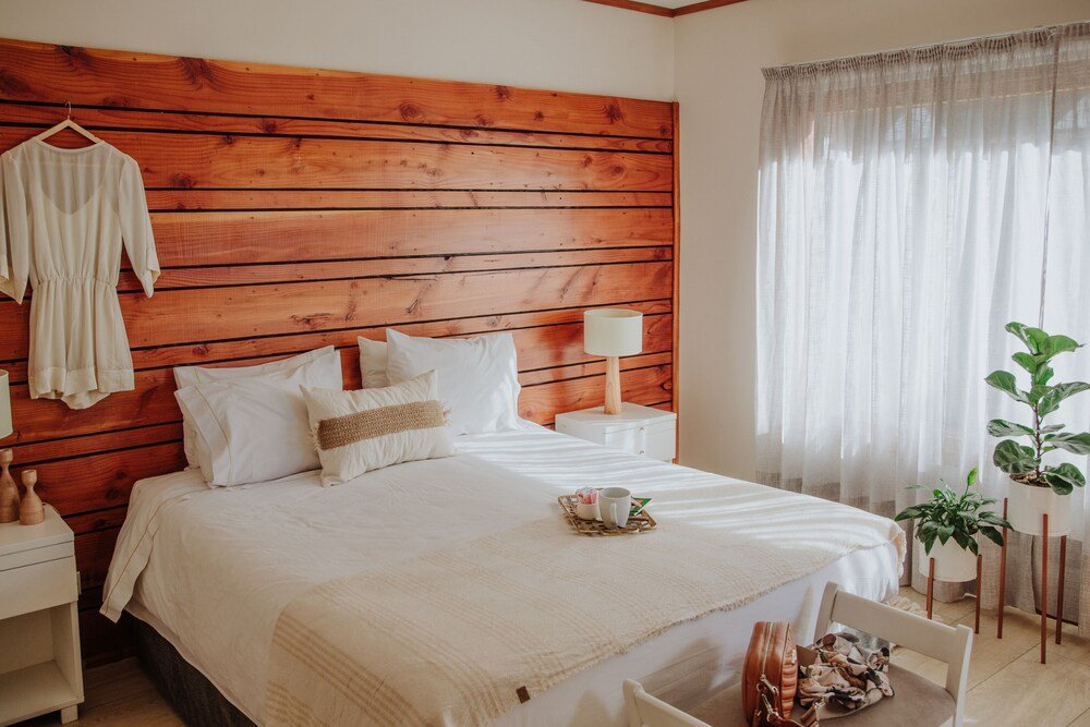 Dormitorio con respaldo de madera, ropa de cama blanca y mesa de luz