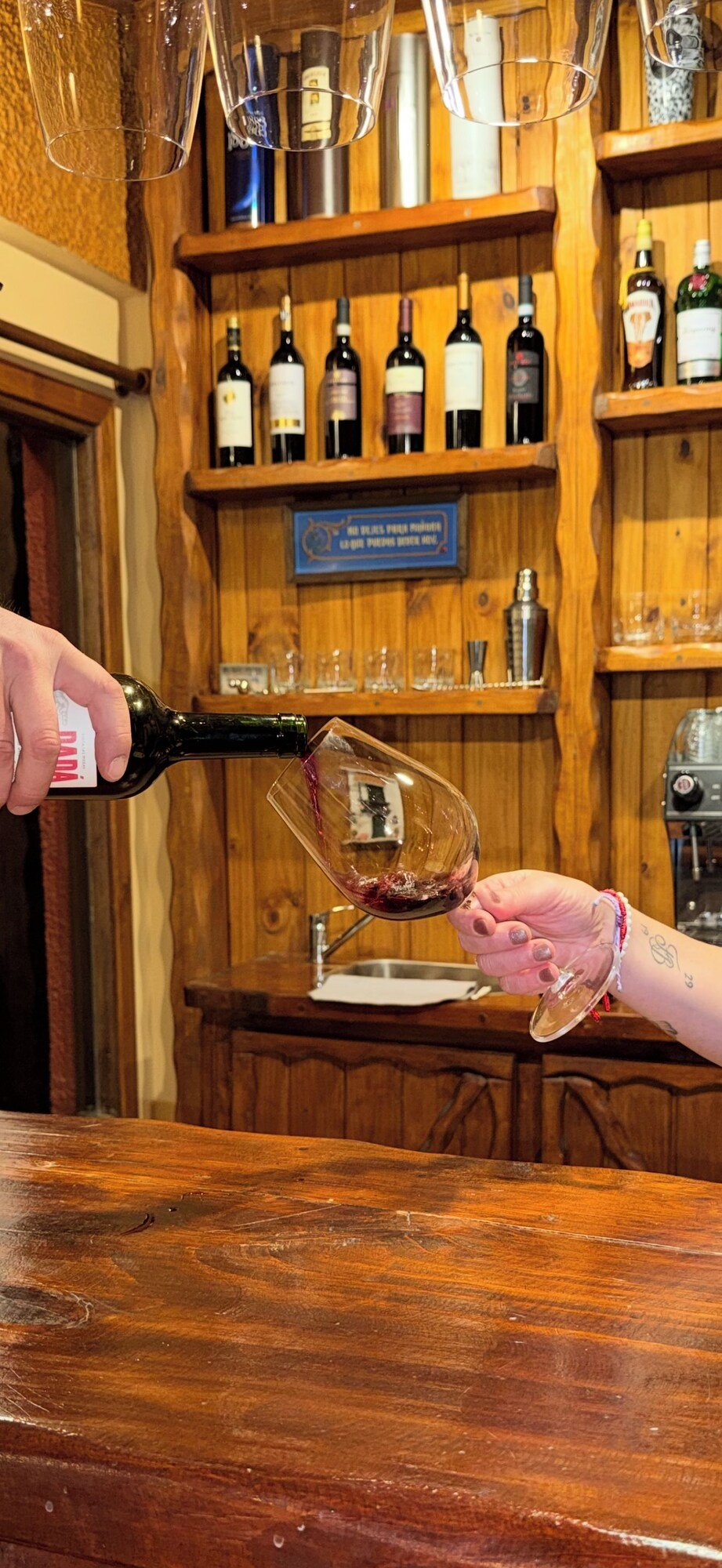 Person pouring wine into a glass at a bar with wooden shelves