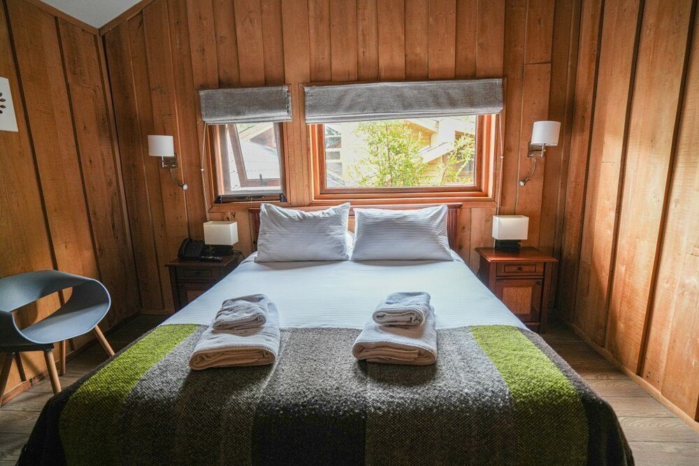 Habitación revestida en madera con cama y dos lámparas de mesa de luz