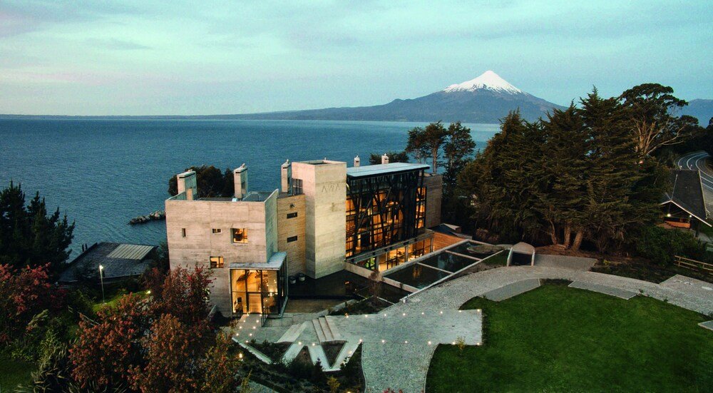 Modern glass-fronted hotel building with lake and mountain behind