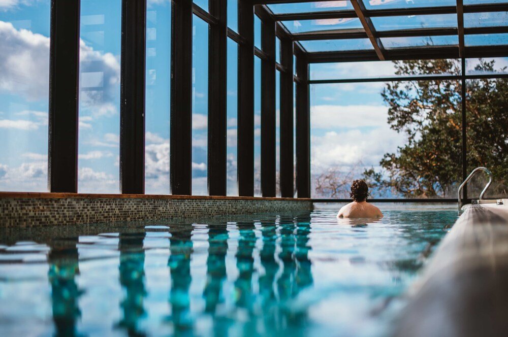 Swimmer in a clear blue indoor pool beside tall windows