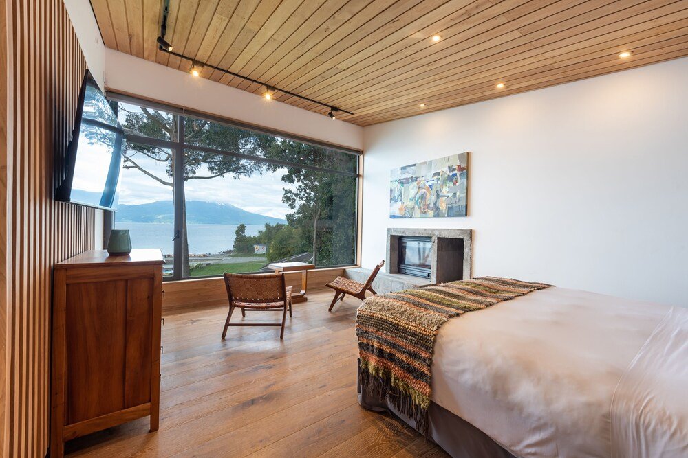 Bedroom with large window, wooden flooring, fireplace and outdoor view