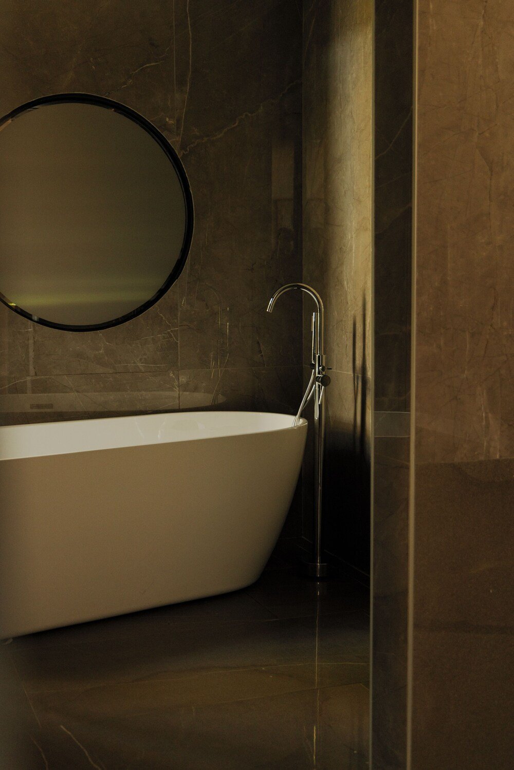 Bathroom with freestanding bathtub, round mirror and sleek faucet