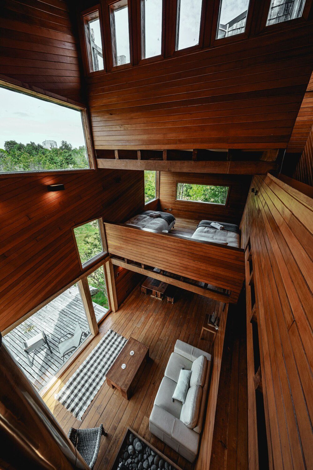 Cabaña con dormitorio tipo altillo, sofá y comedor con vista al exterior