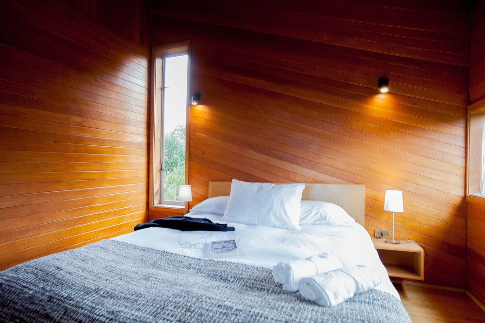 Wood-panelled bedroom with white bedding, nightstand and lamp
