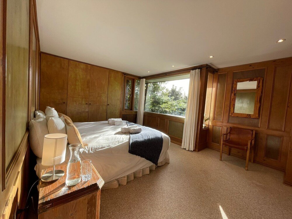 Spacious bedroom with large bed, lamp, chair and view of greenery