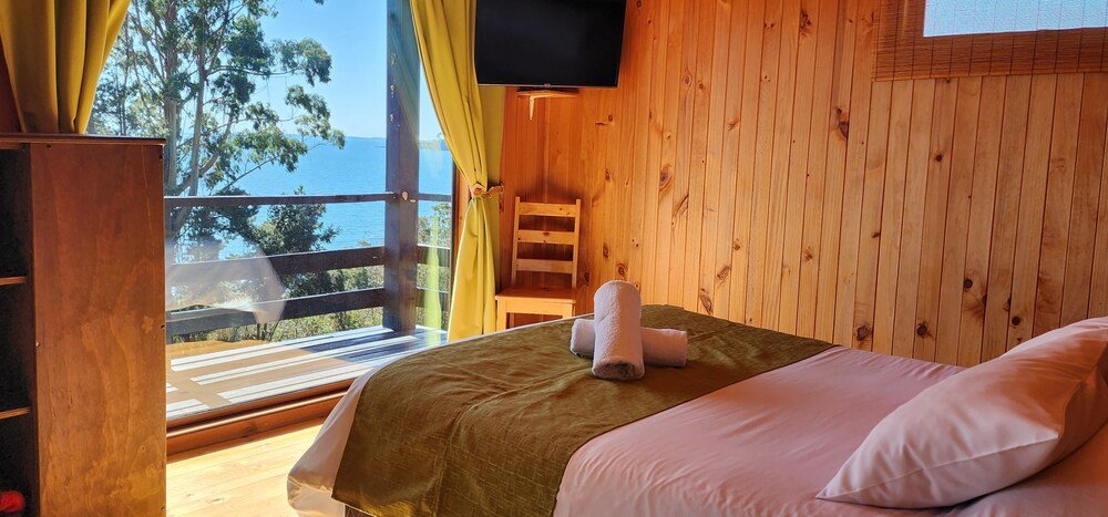 Habitación de cabaña de madera con cama, TV y balcón con vista al mar