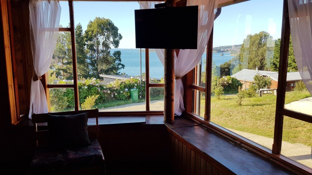 Habitación con gran ventana hacia el agua, la vegetación y edificios lejanos