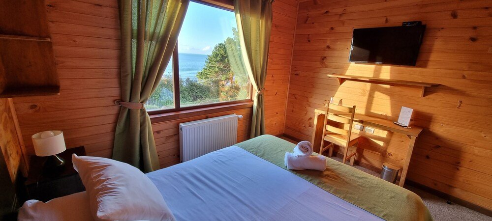 Habitación de cabaña de madera con cama, escritorio, TV y ventana con cortinas