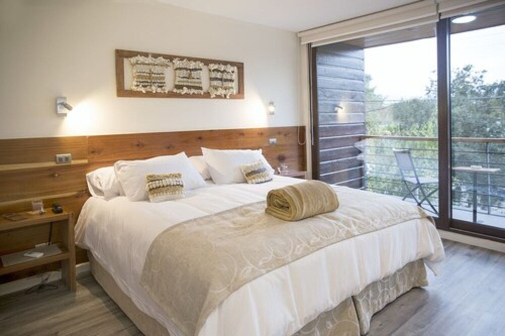 Bedroom with wooden headboard, artwork and balcony with table and chairs