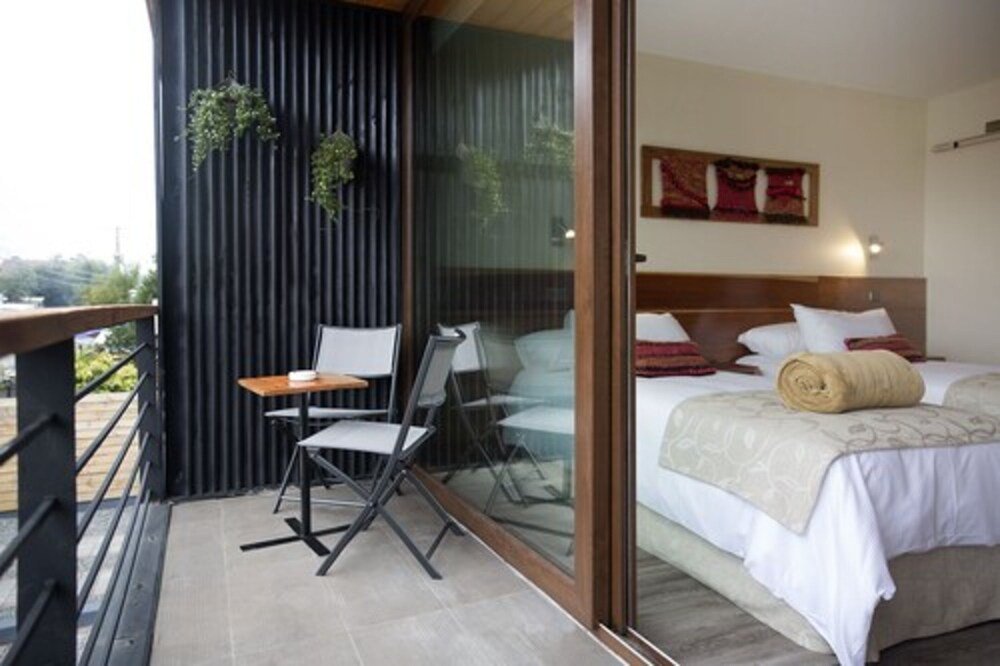 Modern hotel room with balcony, white linens and wooden headboard
