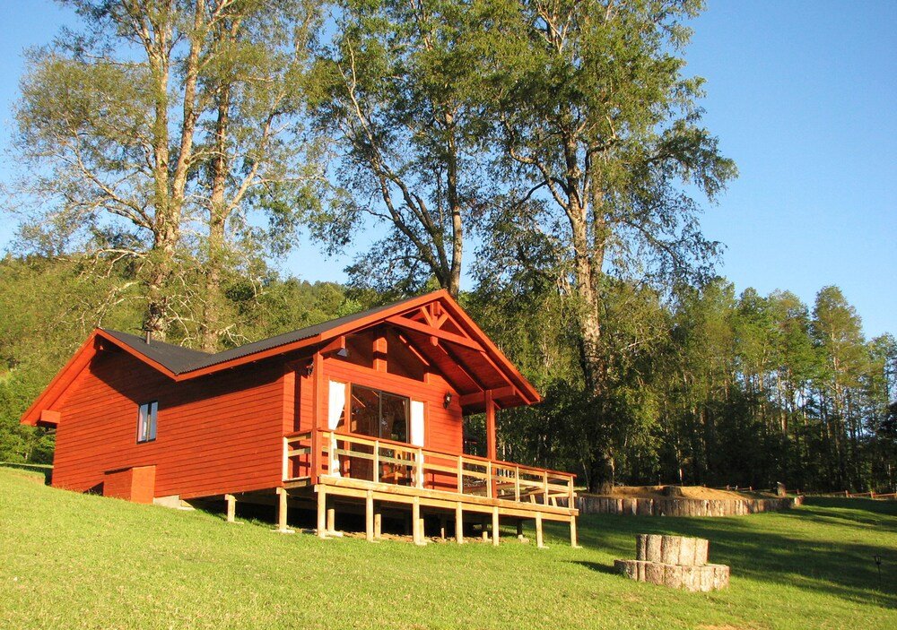 Red wooden cabin with balcony among grass and trees