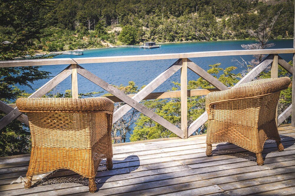 Wooden deck with two wicker chairs overlooking a lake and a boat