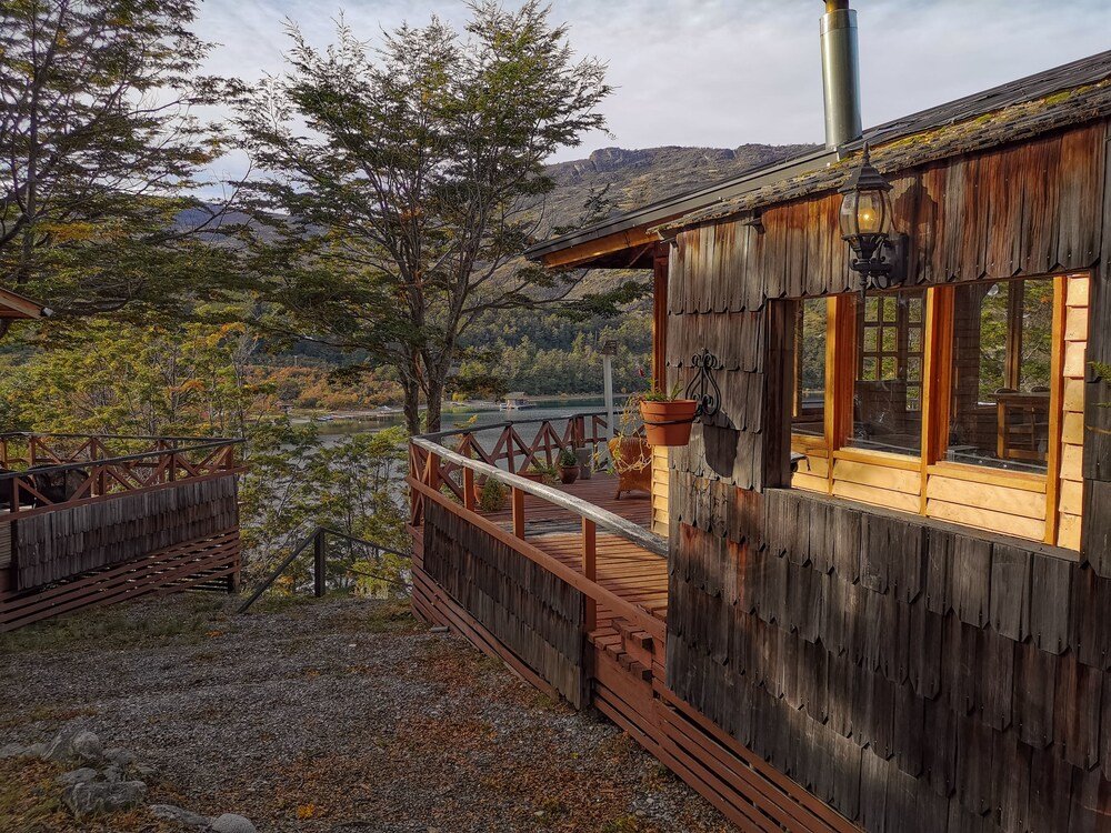 Rústica cabaña de madera con balcón sobre un lago y colinas boscosas