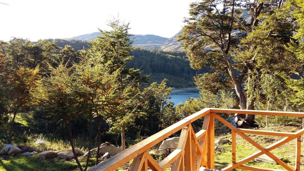 Terraza de madera frente a un lago rodeado de árboles y colinas
