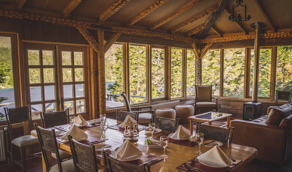 Comedor con muebles de madera, grandes ventanales y chimenea de piedra