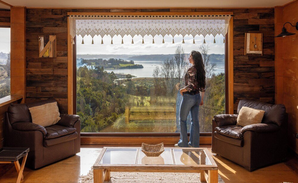 Sala con gran ventana sobre un lago y colinas, sofás de cuero