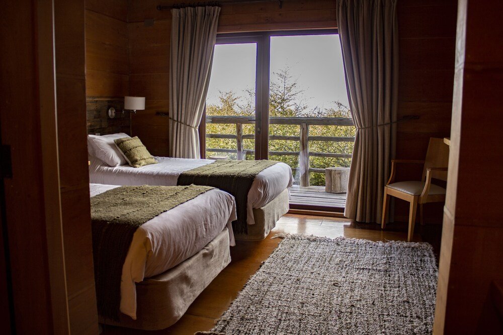 Habitación con dos camas, piso de madera y ventanal hacia los árboles
