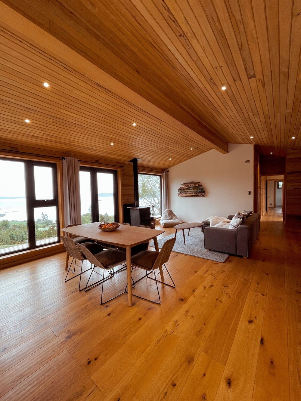 Salón amplio con techo de madera, ventanales, comedor y chimenea