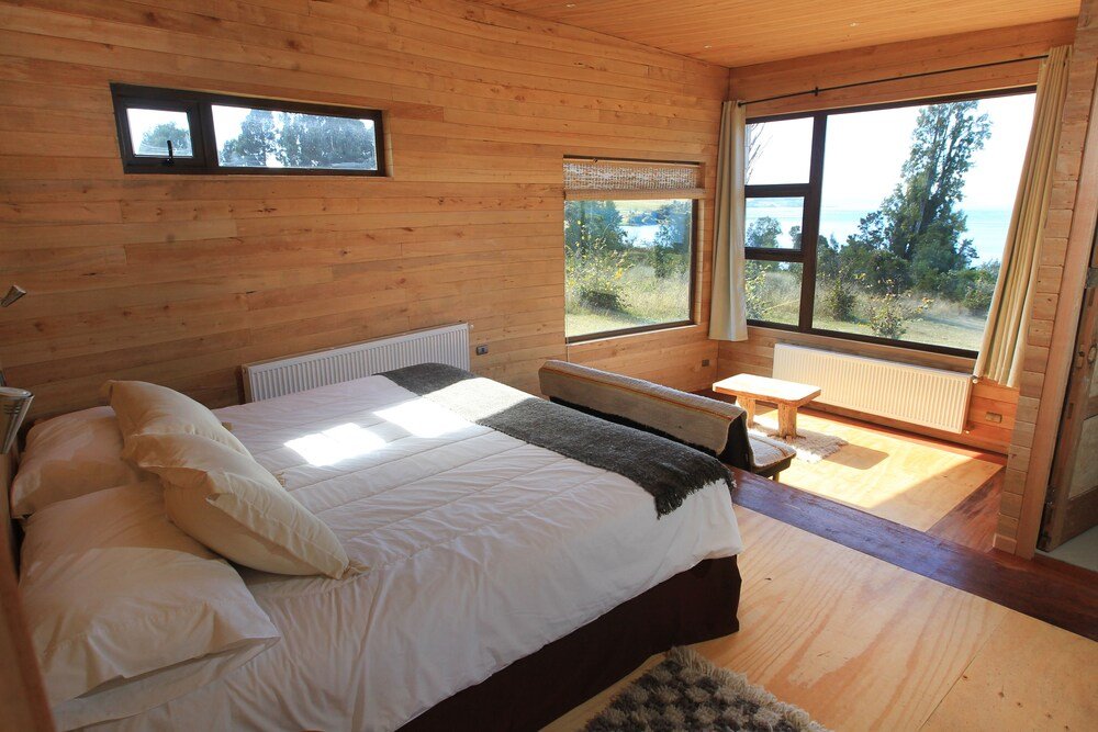 Dormitorio revestido en madera con cama grande, mesa pequeña y vista exterior