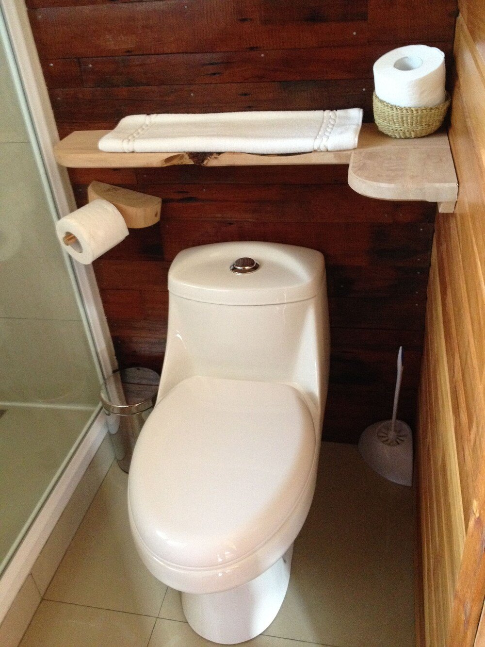 Baño pequeño con inodoro blanco y estante de madera encima