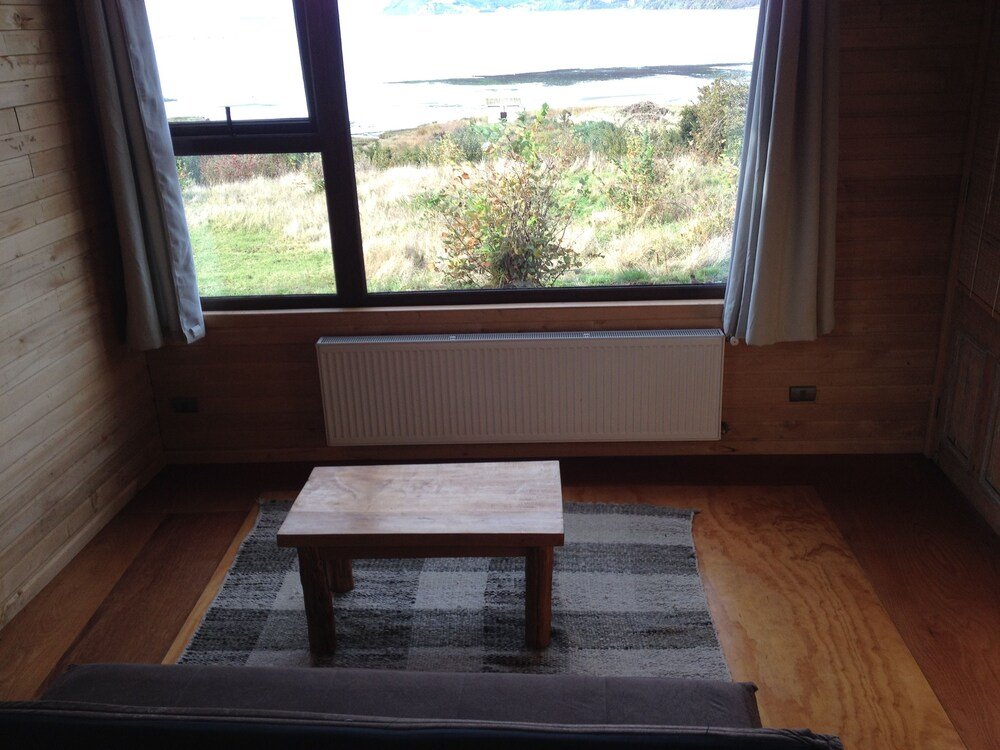 Habitación con piso de madera, mesa pequeña, radiador y ventana al paisaje