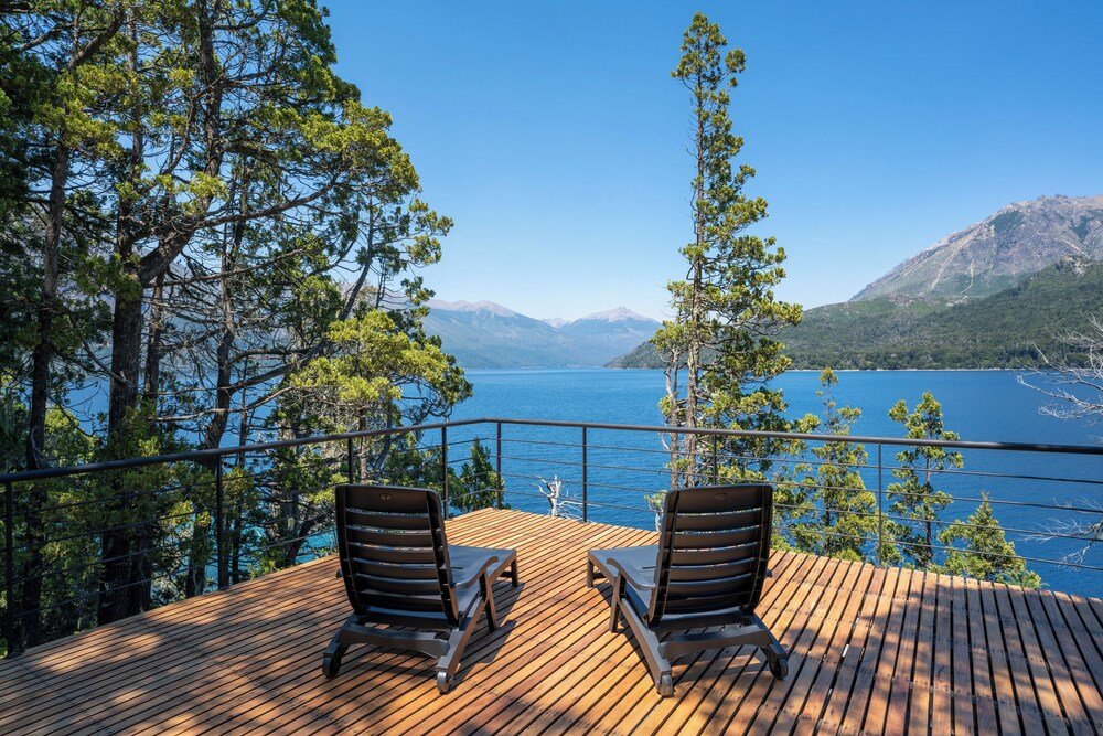 Deck de madera con dos reposeras frente a un lago y montañas