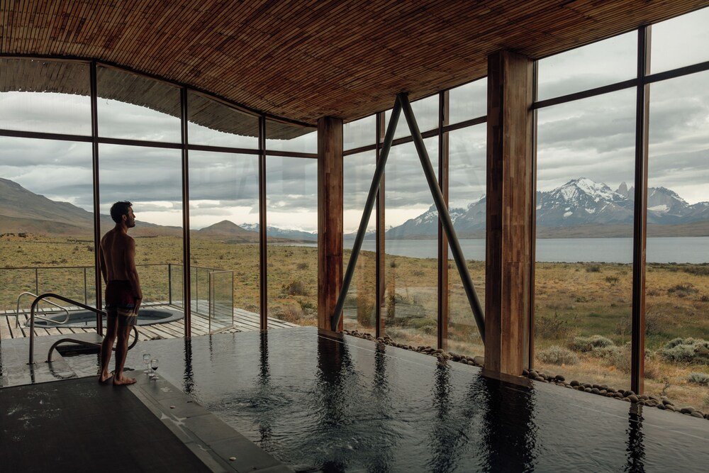 Man standing by a large indoor pool with mountain and lake views