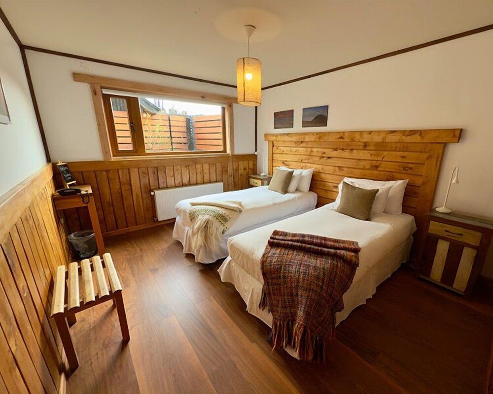 Room with two beds, a wooden bench and a small table